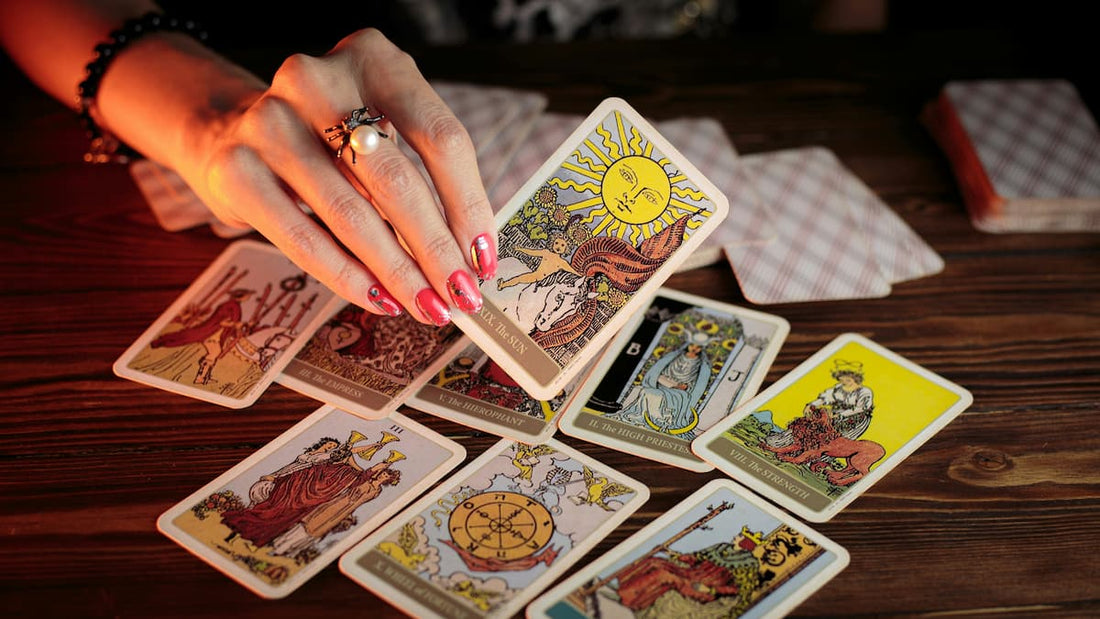 Mão segurando uma carta de tarot sobre a mesa com várias cartas espalhadas, representando o processo de leitura de tarot e interpretar seus significados.