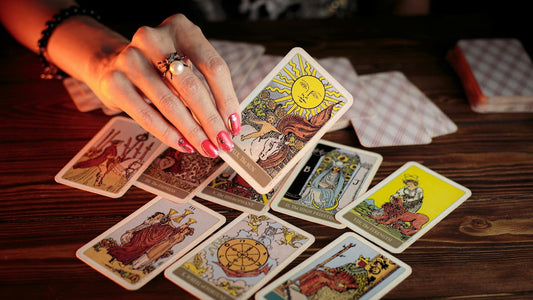 Mão segurando uma carta de tarot sobre a mesa com várias cartas espalhadas, representando o processo de leitura de tarot e interpretar seus significados.